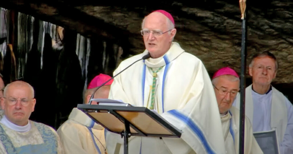 Graphic of Archbishop Farrell wearing a blue and white robe and pink skullcap speaking at the Grotto in Lourdes. In the background are other archbishops.