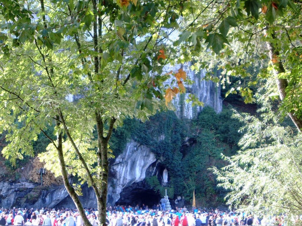 Pilgrims gathered at the Lourdes grotto with the statue of Our Lady visible in the cave.