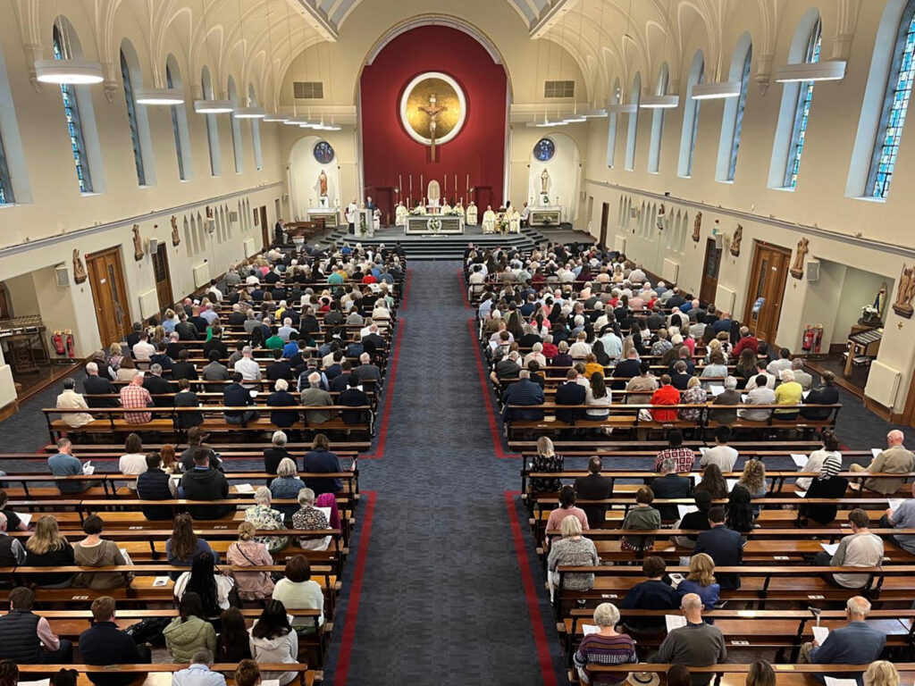 Graphic of the inside of Church of Our Lady Queen of Peace, Merrion Road, Dublin showing the congregation sitting looking up at the altar where there are many clergy people.