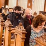 Graphic of the congregation sitting down on the benches in the church with most wearing facemasks. Most people are looking down with their heads bent in prayer.
