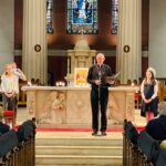 Graphic of a man in a black suit at the altar speaking into a microphone to the congregation.