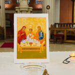 Graphic of a painting of a man, woman and young child seated around a table of food. There is a candle beside the painting.