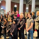 Graphic of a group of people standing with papers in their hands looking towards the altar with white columns and lights in the background.