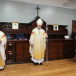 Graphic of Archbishop Dermot Farrell standing in front of a dark brown cabinet with a brown cross and a blue wall in the background.
