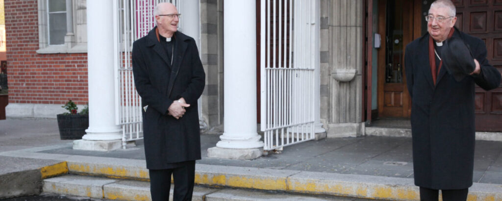 Graphic showing Archbishop Dermot Farrell and Archbishop Diarmuid Martin standing outside of the church in their black priest suits.