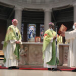 Graphic of a priest handing a book to the His Excellency Archbishop Jude Thaddeus Okolo, Apostolic Nuncio to Ireland with Archbishop Farrell watching in the background.