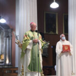 Graphic of Archbishop Dermot Farrell speaking through a microphone wearing his green archbishop's robe with a priest in the background.