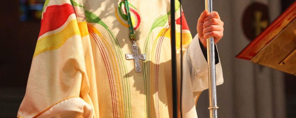 A close-up image of Father Dermot Farrell's silver cross around his neck and his yellow, green and red robe.
