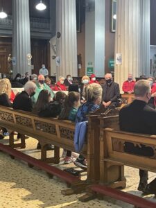 Graphic showing a congregation of people gathered together inside a church on benches with three large white pillars and an altar in the background.