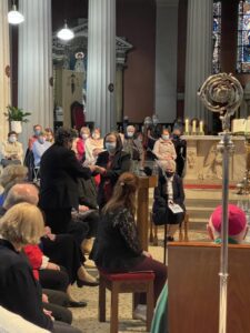 Graphic of a woman standing at the stand to speak and a man passing her an object with the congregation watching them.