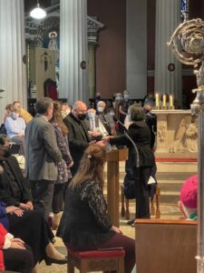 Graphic of a man standing at the stand with a face mask and two other people behind him with a woman placing down an object onto the stand.