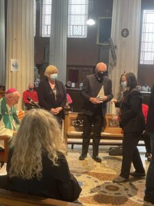 Graphic of Archbishop Dermot Farrell sitting beside a microphone with a woman approaching him, a woman standing beside him and a man standing beside that woman holding a Synod boat.