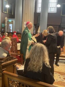 Graphic of Archbishop Dermot Farrell standing to speak to the woman and the man and woman beside them bowing their heads in prayer.