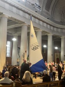 Graphic of a group of young people, a man and woman and Archbishop Dermot Farrell raising a blue and white flag with the congregation watching the display.