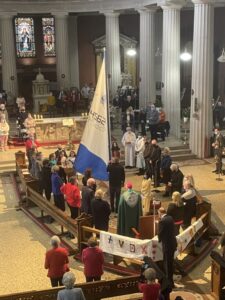 Graphic showing everyone standing up once the flag has been raised with their hands joined together in prayer.