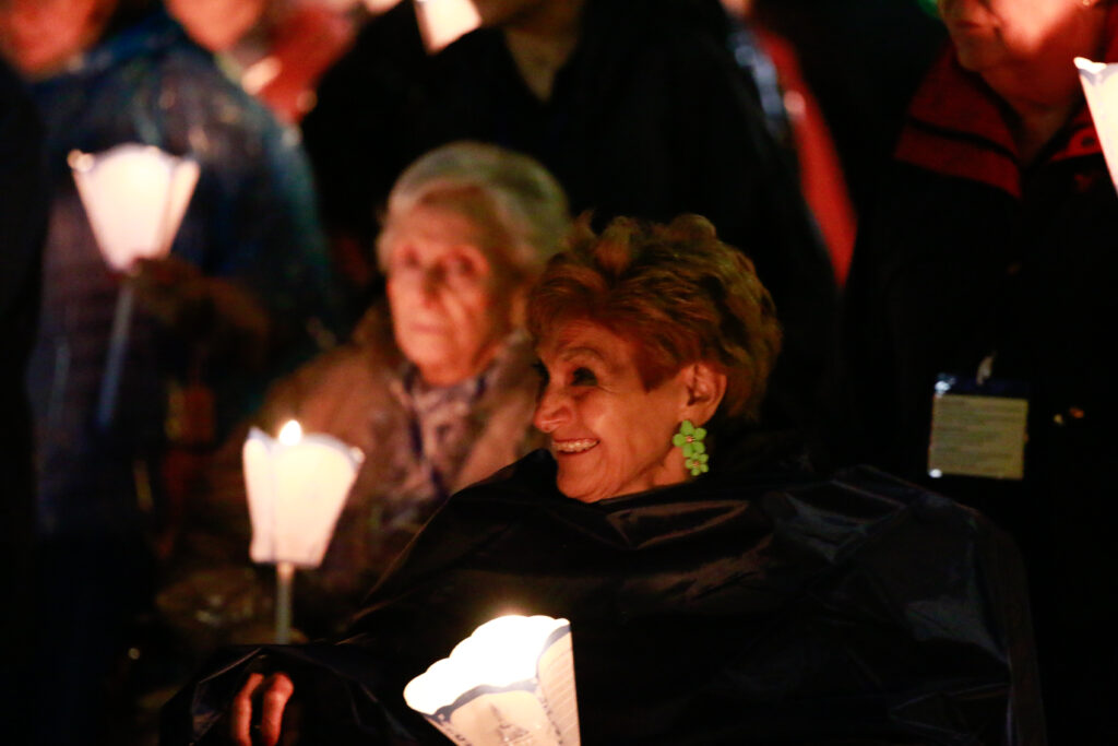 Graphic of a group of people standing together holding lights and smiling. They are wearing winter clothes.