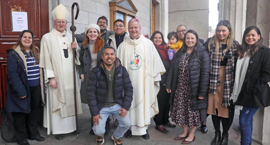 Graphic of a group of people with an archbishop and Archbishop Farrell getting their photo taken and smiling at the camera. The two archbishops are wearing white robes and headpieces.