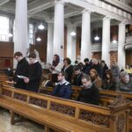 Graphic of the congregation bowing their heads in prayer while some people are still returning to their seats.