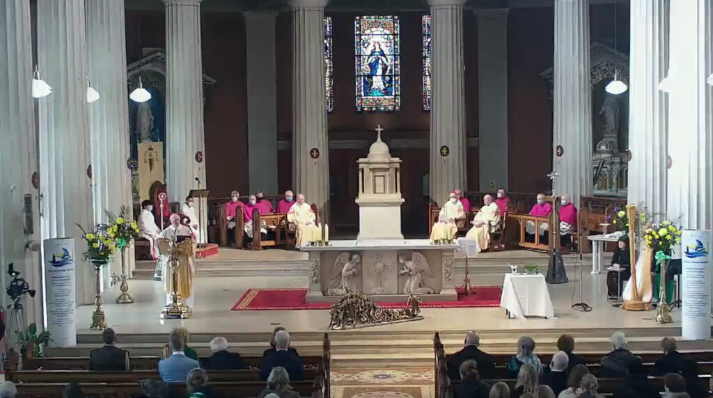 Graphic of a celebration of the Eucharist in St. Mary's Pro-Cathedral in 2022 where there are many Fathers seated on the altar with Archbishop Dermot Farrell delivering his homily from the stand. There are stained glass windows in the background and flowers and Synod signs to each side of the altar.