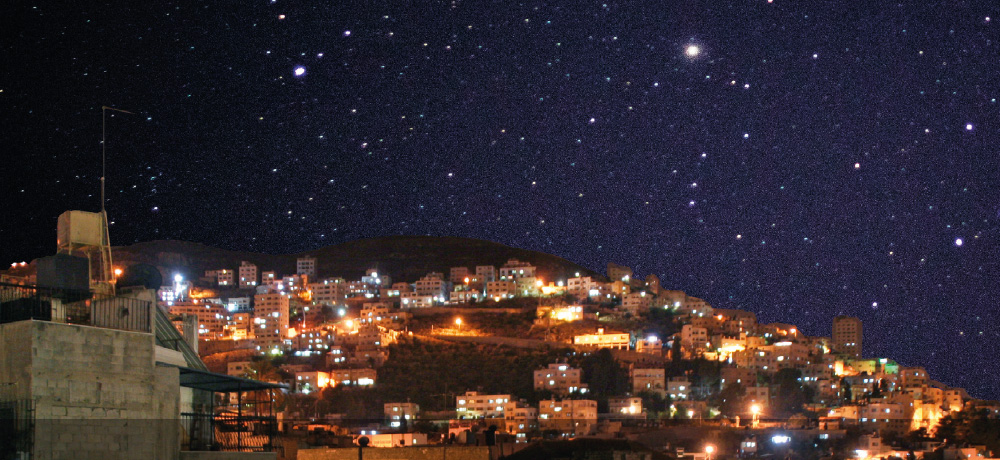 City at night – Lit-up hillside city beneath a starry sky.