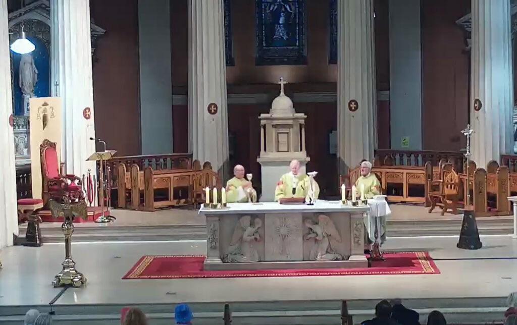 Graphic for the homily of Archbishop Farrell in which Archbishop Farrell is pictured with two other archbishops in green robes standing at the altar taking part in the Eucharist.