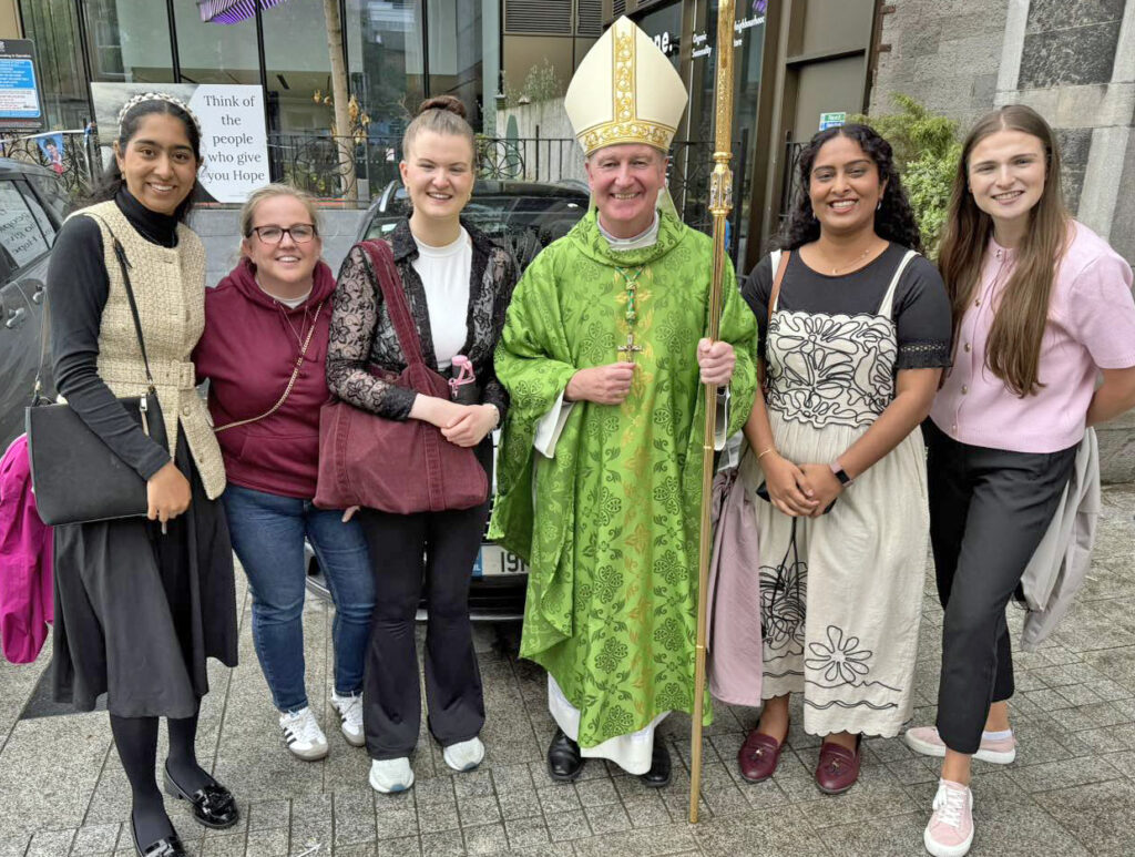 Picture of Bishop Dempsey at City Quay Church with a group of people getting their photo taken. Bishop Dempsey is wearing a green robe and headpiece and holding a staff. The people are smiling at the camera.