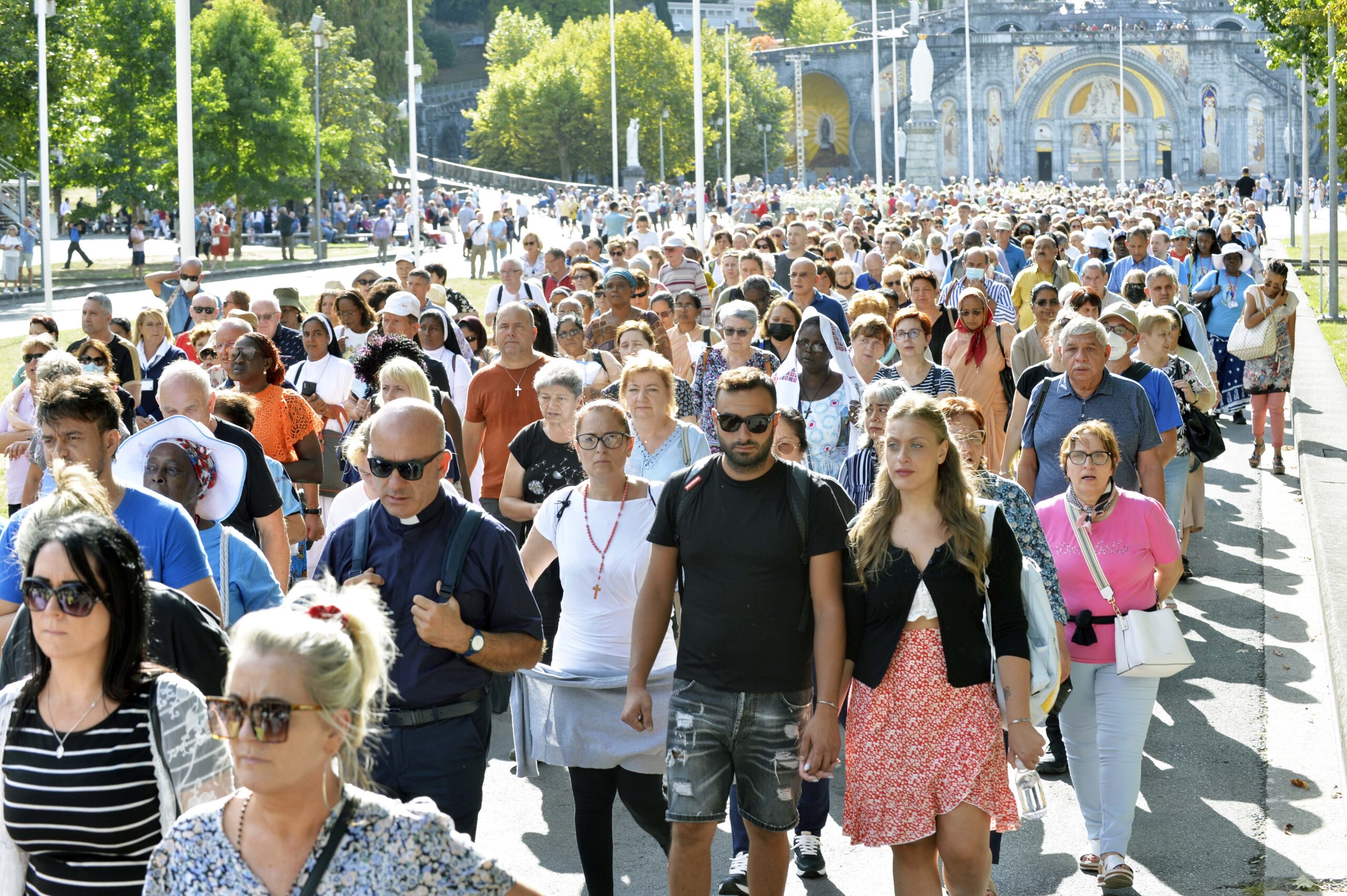 Graphic of a large group of people on the September pilgrimage walking with Lourdes Cathedral in the background.