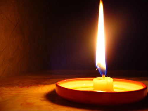 Graphic of a single lit candle on a tray on a wooden board with darkness in the background.